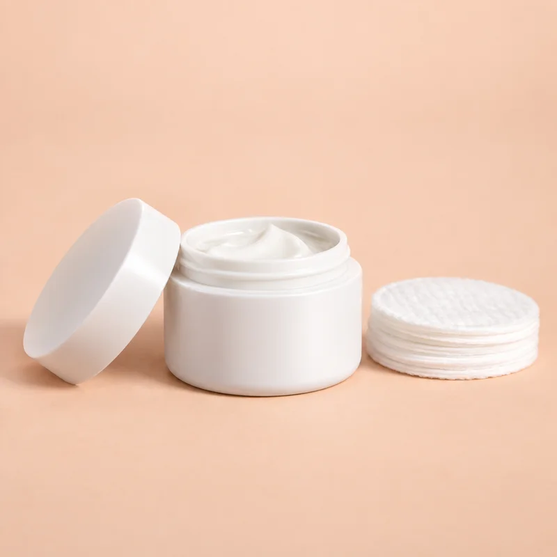 White cream jar and cotton pads on a soft peach background